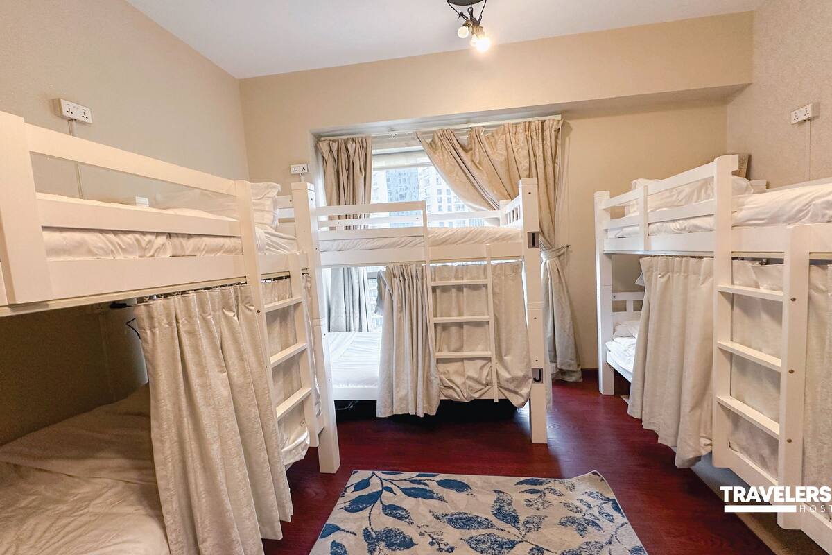 A hostel room with bunk beds, a red carpet, and a window with curtains.