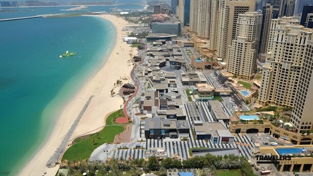 An aerial view of a coastal city with high-rise buildings, a beach, and a marina. - Travelers Dubai Marina Hostel (Dubai)