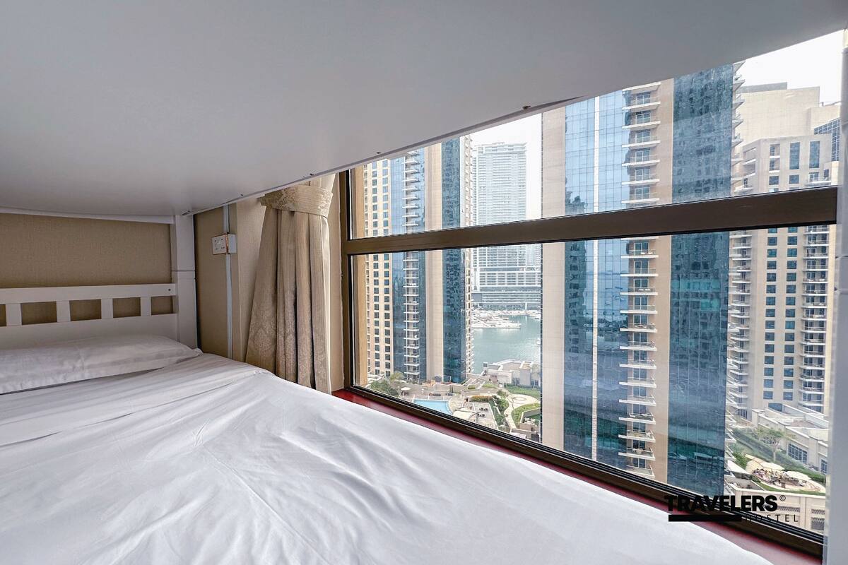 A hotel room with a large bed, a headboard, and a window with a view of high-rise buildings.