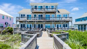 A multi-story beachfront building with a wooden deck and railings leading to the entrance. - Oceanfront home with stunning views, designed for comfort (Emerald Isle)