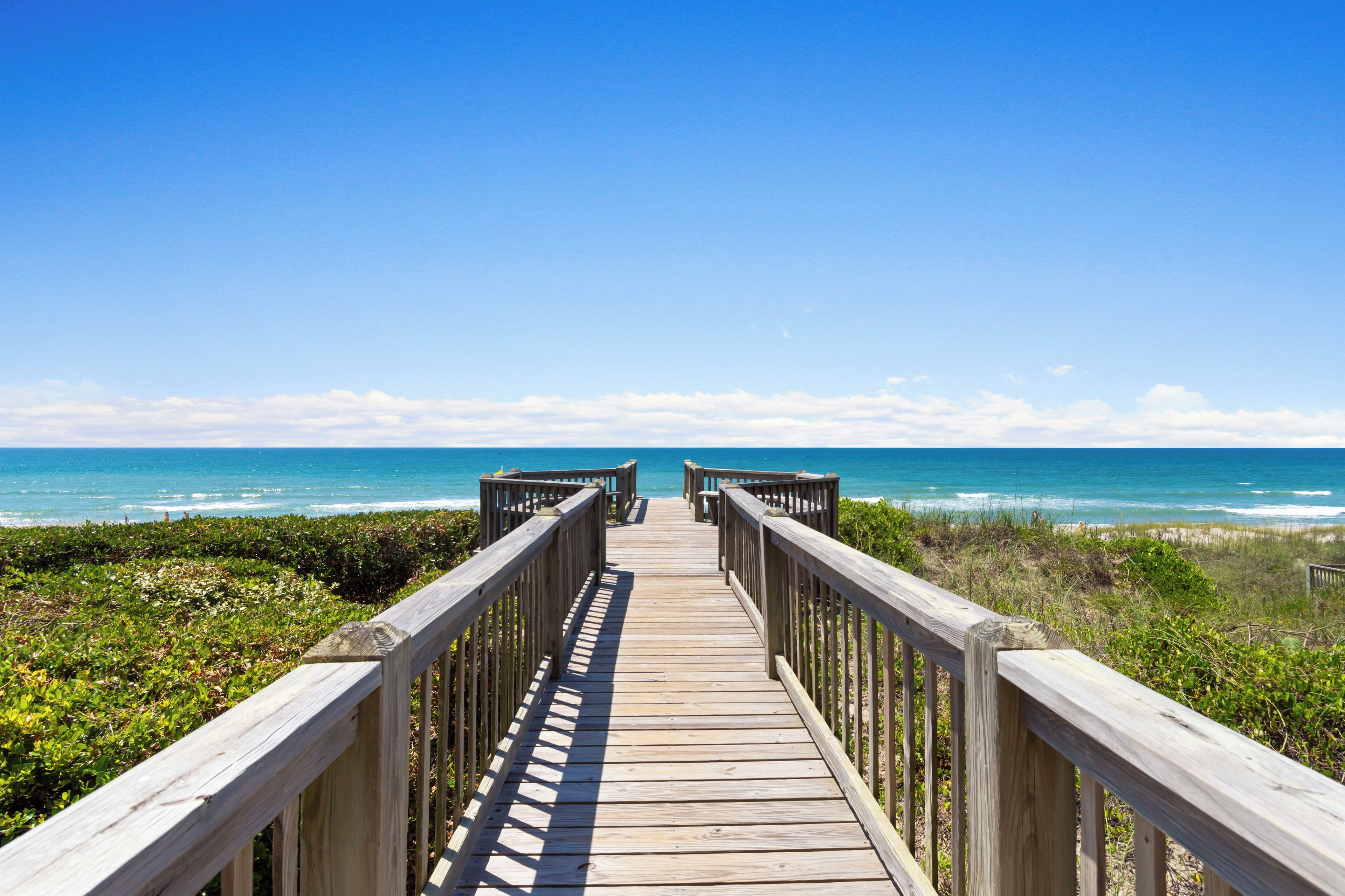 A wooden boardwalk leading to the beach with a clear view of the ocean.