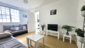 Un salon moderne avec un canapé, un téléviseur posé sur un meuble, une table basse et des plantes en pot.