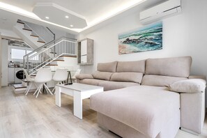 Un salon moderne avec un canapé, une table à manger et des chaises. Un escalier mène à l’étage supérieur.