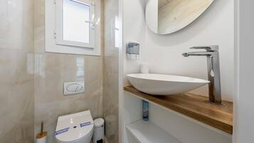 Un baño moderno con inodoro, bidé, lavamanos, espejo y ventana.