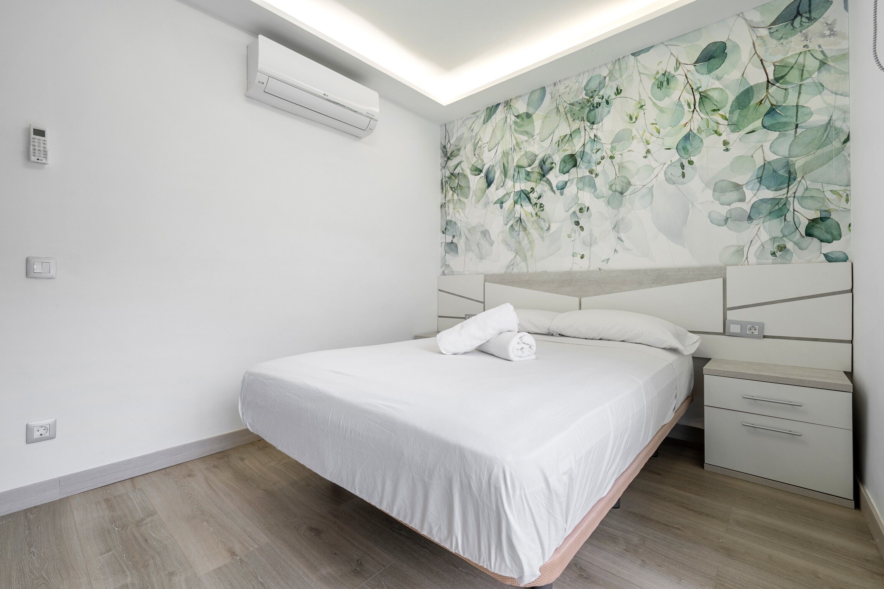 Een moderne slaapkamer met een bed, nachtkastje, airconditioner en een muur met een bladerpatroon.