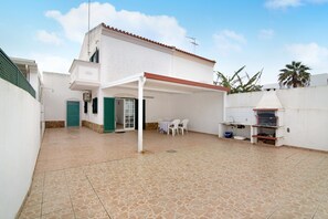 A covered patio area with a grill, outdoor seating, and a door leading to a covered entrance.