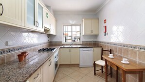 A kitchen with cabinets, a sink, a dishwasher, a stove, and a dining table with chairs. - Holiday Home 'Moradia Altura' with Private Terrace and Balcony (Altura)