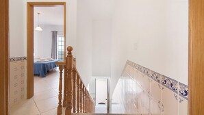A staircase with a wooden handrail, a tiled wall with a decorative border, and a bedroom with a bed and a window. - Holiday Home 'Moradia Altura' with Private Terrace and Balcony (Altura)