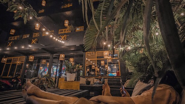 A person relaxing on a lounge chair in an outdoor setting with string lights overhead. - Sugar Hostel Weligama  (Weligama)