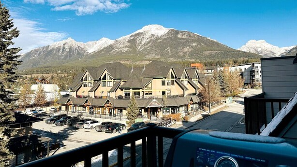 A hotel with a mountain backdrop, featuring a parking lot and a view of snow-capped peaks.