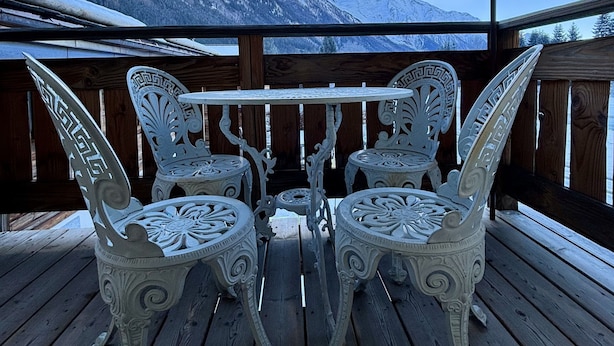 Een houten terras met decoratieve witte stoelen en een tafel, met uitzicht op een besneewd berglandschap.