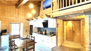 Een houten interieur met een eettafel, stoelen, een keuken met witte kastjes en een vide met uitzicht op het landschap.