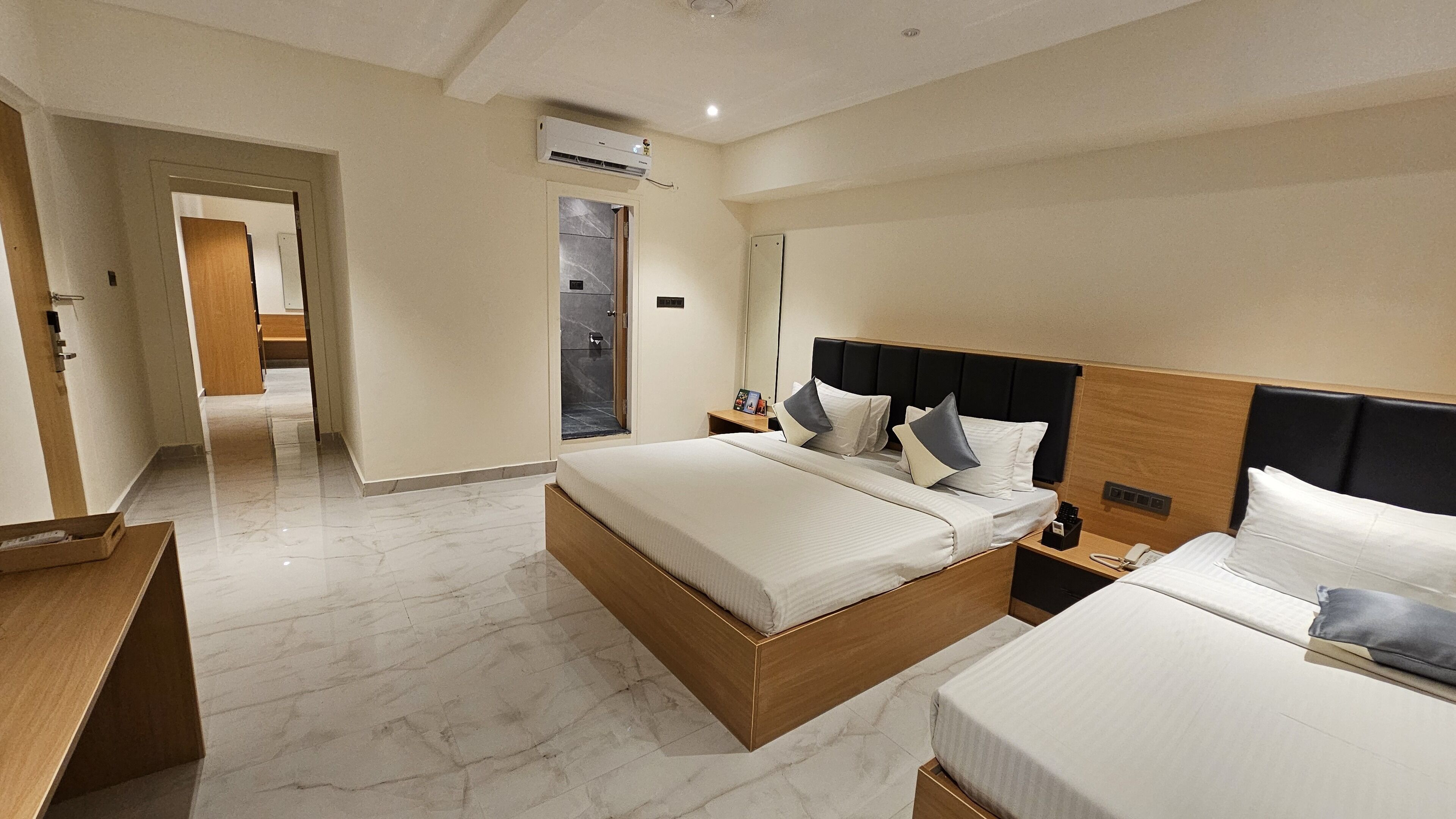 Une chambre d’hôtel avec un grand lit, un lit plus petit, une table de chevet, une commode, un miroir et une porte donnant sur une salle de bain.