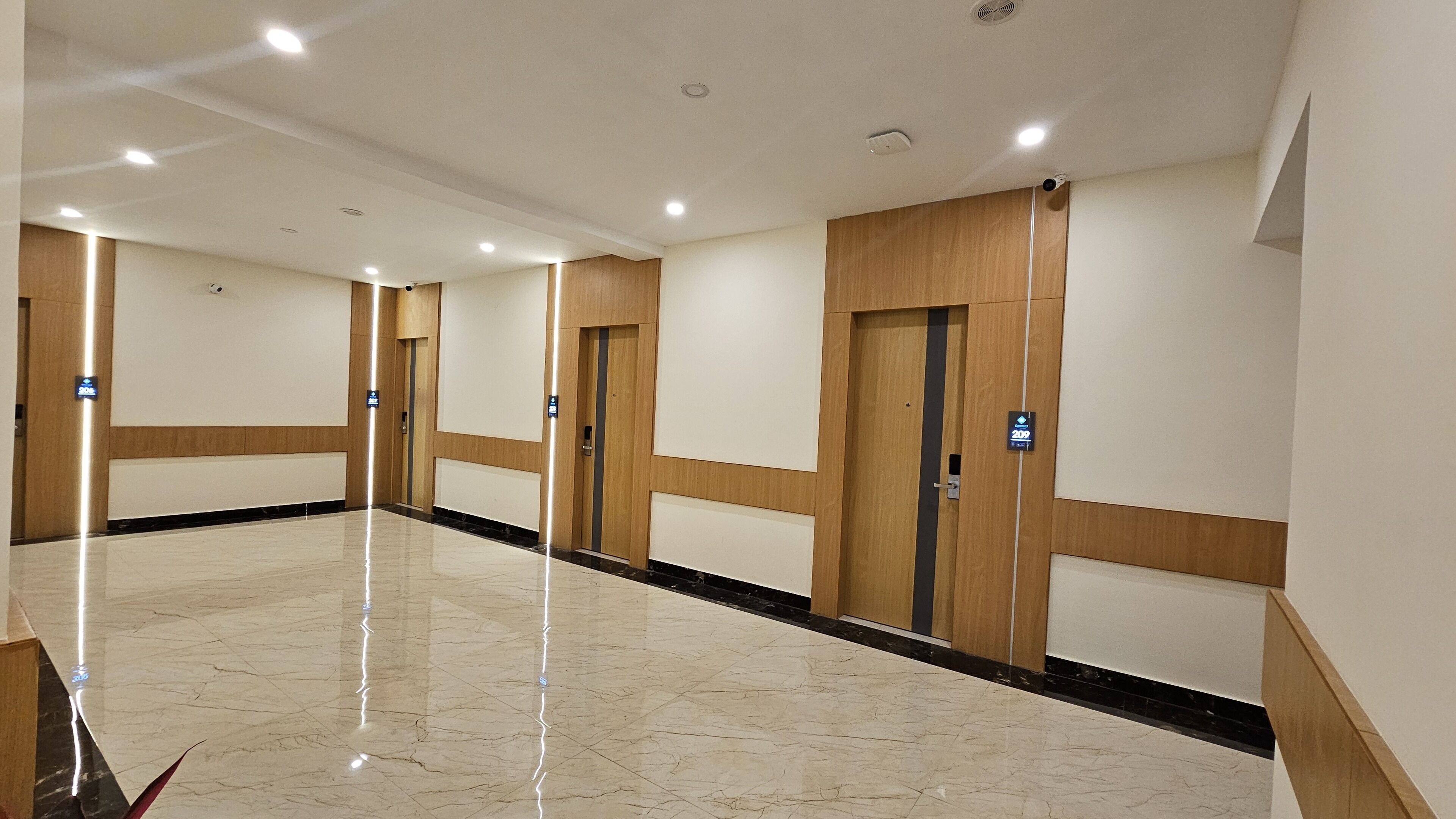 A hotel corridor with wooden paneling, marble flooring, and doors marked with room numbers.