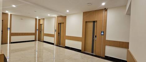 A hotel corridor with wooden paneling, marble flooring, and doors marked with room numbers.
