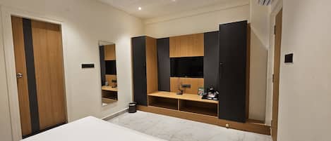 A hotel room with a bed, a mirror, a wardrobe, and a shelf with toiletries.