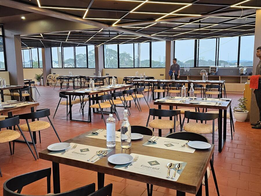 A spacious dining area with multiple tables set for guests, large windows offering views of the outdoors, and a modern ceiling design.