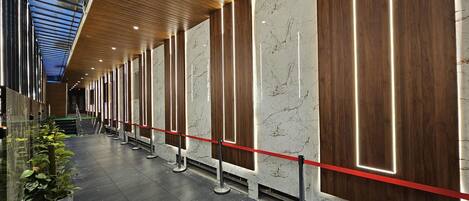 A modern hotel lobby with a long corridor, marble walls, and a wooden ceiling.