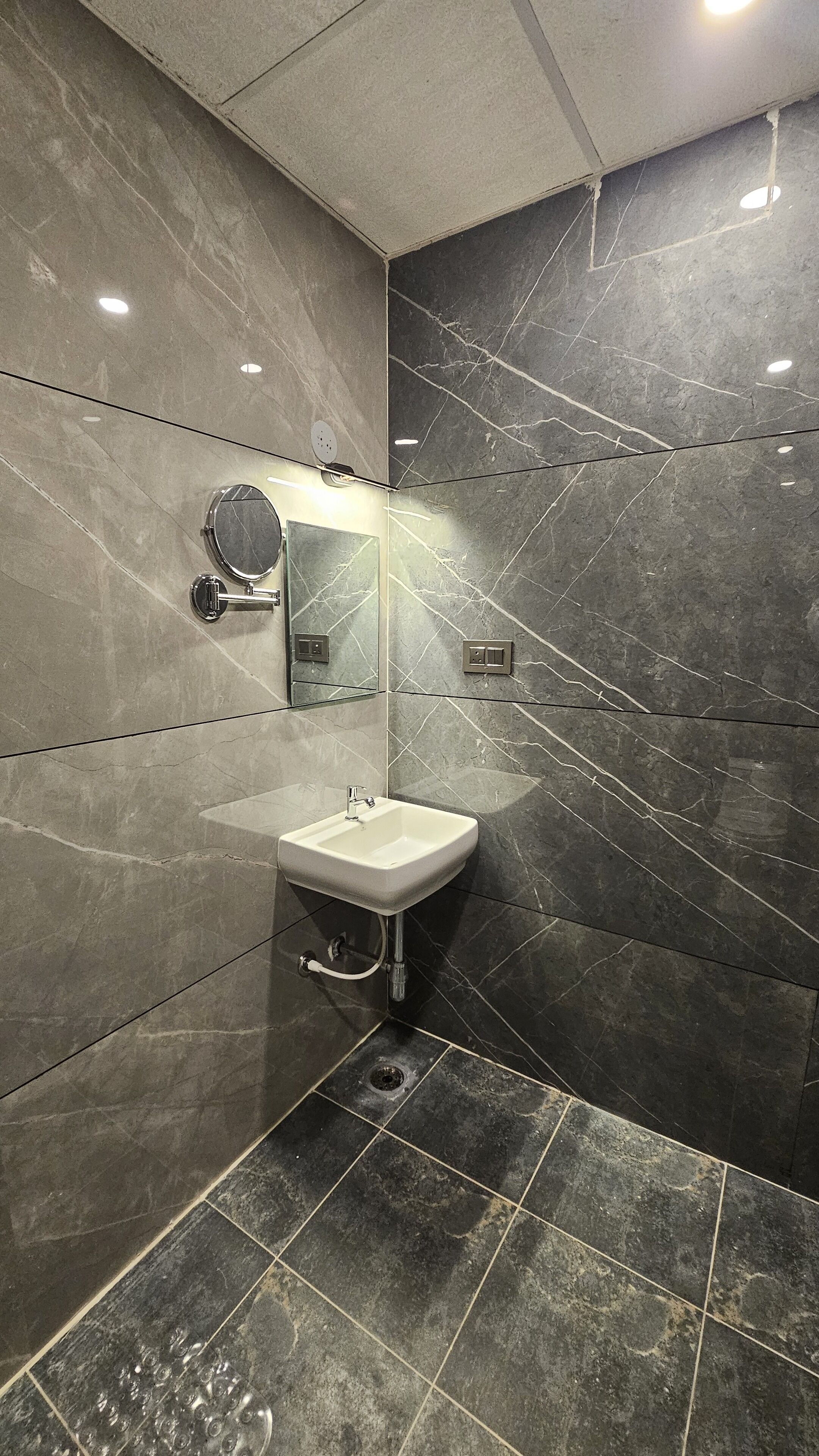 A modern bathroom with a sink, mirror, and dark marble tiles.