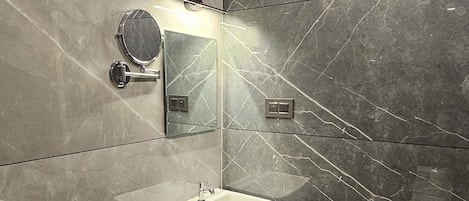 A modern bathroom with a sink, mirror, and dark marble tiles.