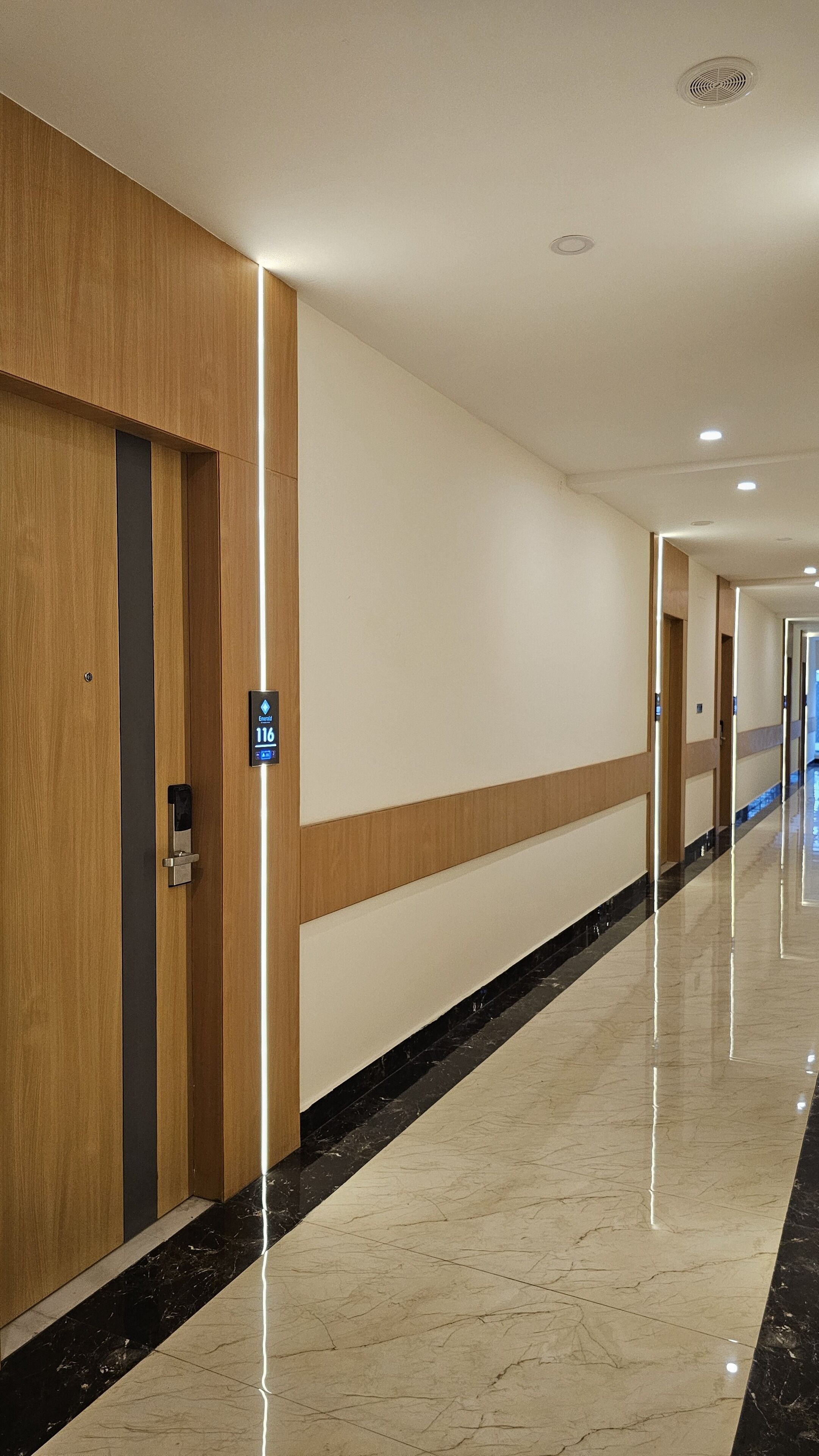 A hotel corridor with wooden paneling, a marble floor, and a sign indicating room number 116.