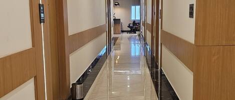 A long, well-lit hallway with a shiny marble floor, wooden paneling on the walls, and a trash can on the left.