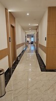 A long, well-lit hallway with a shiny marble floor, wooden paneling on the walls, and a trash can on the left.