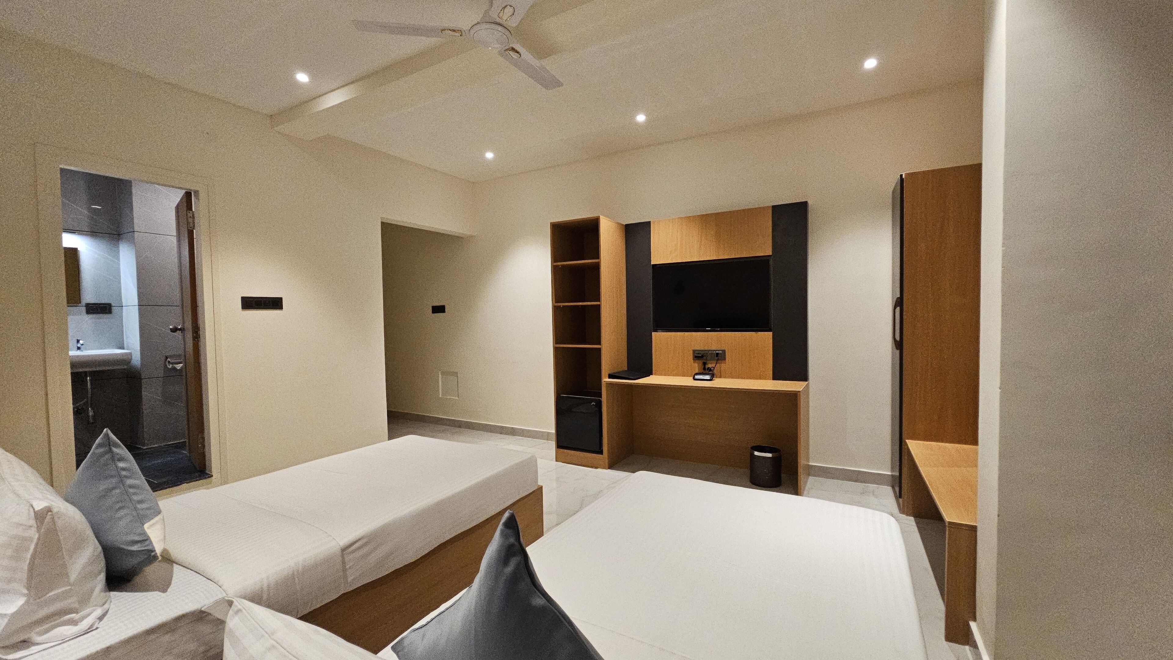 A modern hotel room with two single beds, a built-in wardrobe, a vanity with a mirror, and a small seating area.