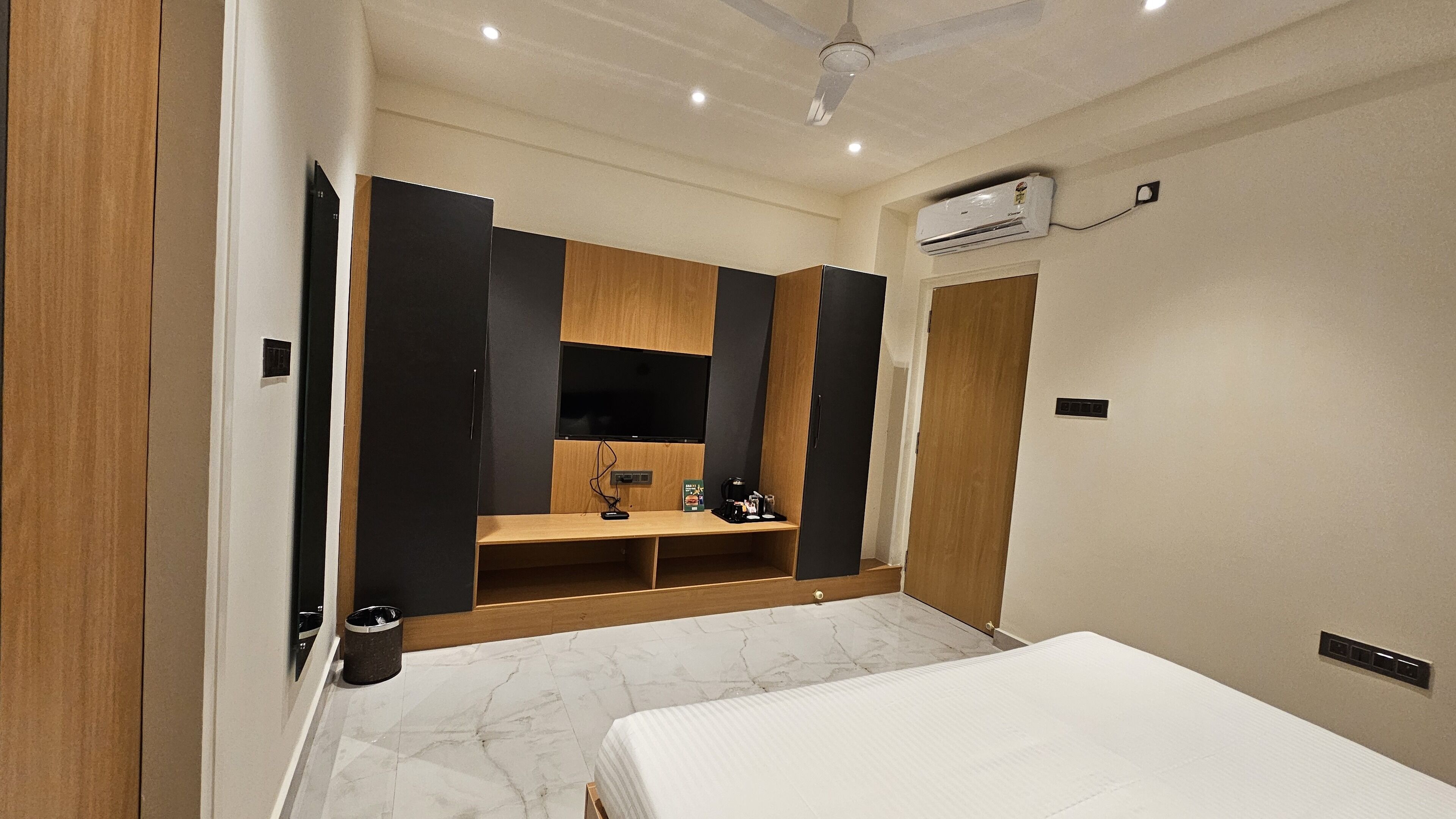 A hotel room with a bed, a vanity with a mirror, a small desk with a chair, and a wardrobe.