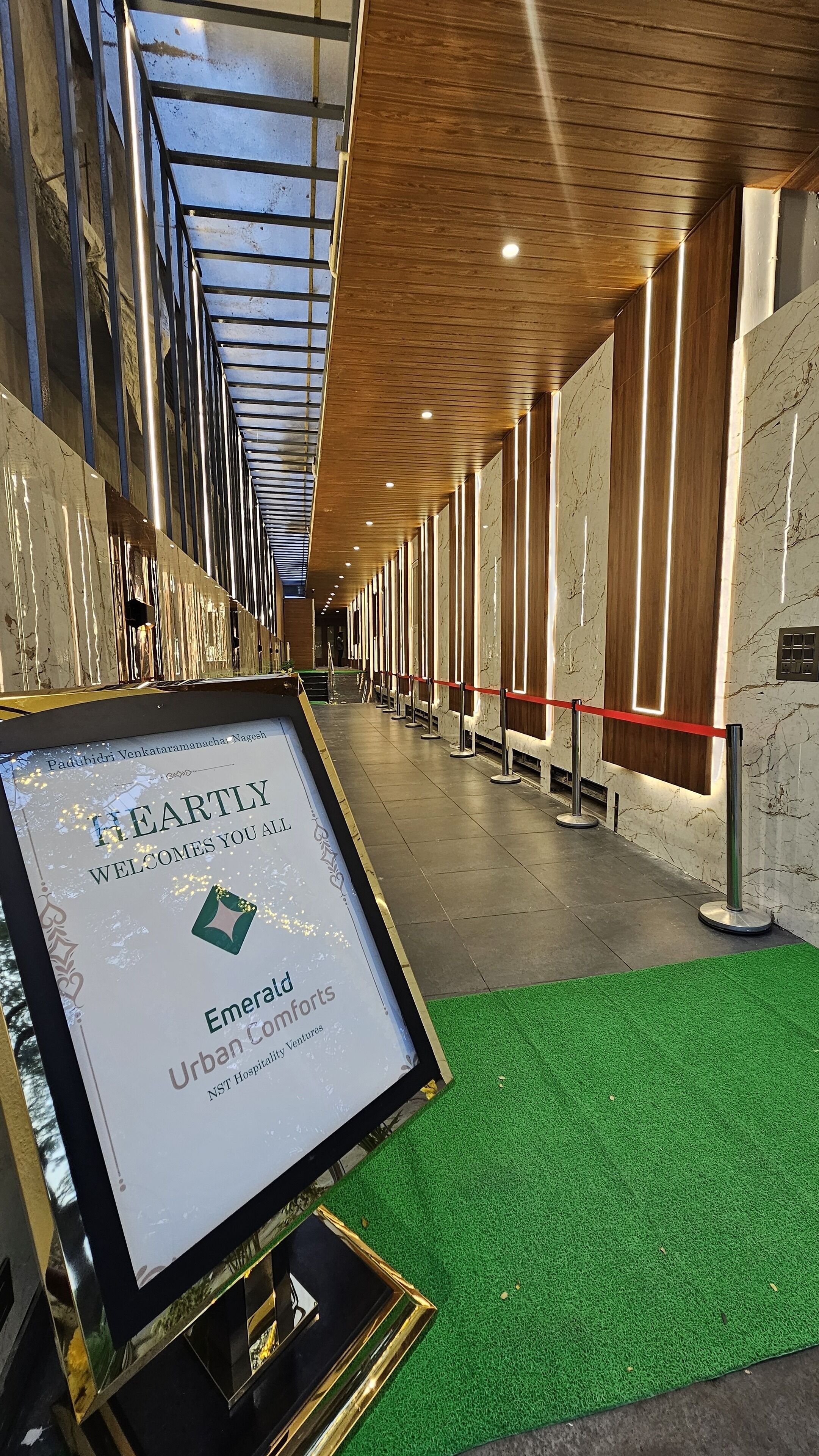 Un couloir orné d’une enseigne encadrée portant l’inscription « Emerald Urban Comforts » et recouvert d’une moquette verte.