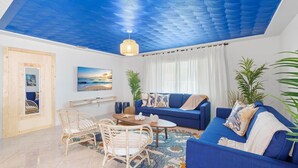 A living room with a blue ceiling, a blue sofa, a wooden coffee table, wicker chairs, and a large window with curtains. - Santorini · Casa Santorini - Big Pool, BBQ & Free Parking (Miami)