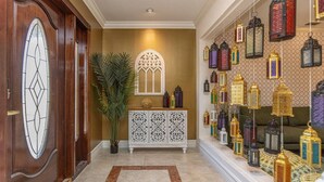 Un couloir avec une porte en bois, une grande fenêtre, un meuble décoratif blanc et un mur orné de lanternes suspendues.