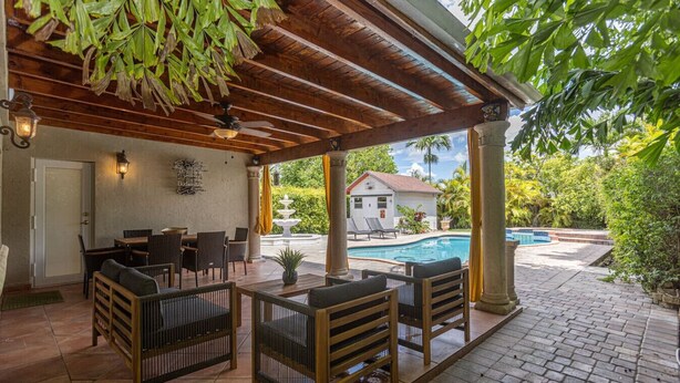 Une terrasse extérieure avec des meubles en bois, une piscine et un bâtiment blanc en arrière-plan.
