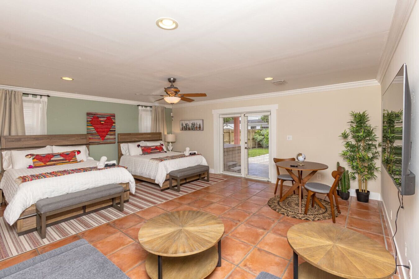 Une chambre d’hôtel avec deux lits, un ventilateur de plafond, un coin repas avec une table et des chaises, et un téléviseur fixé au mur.