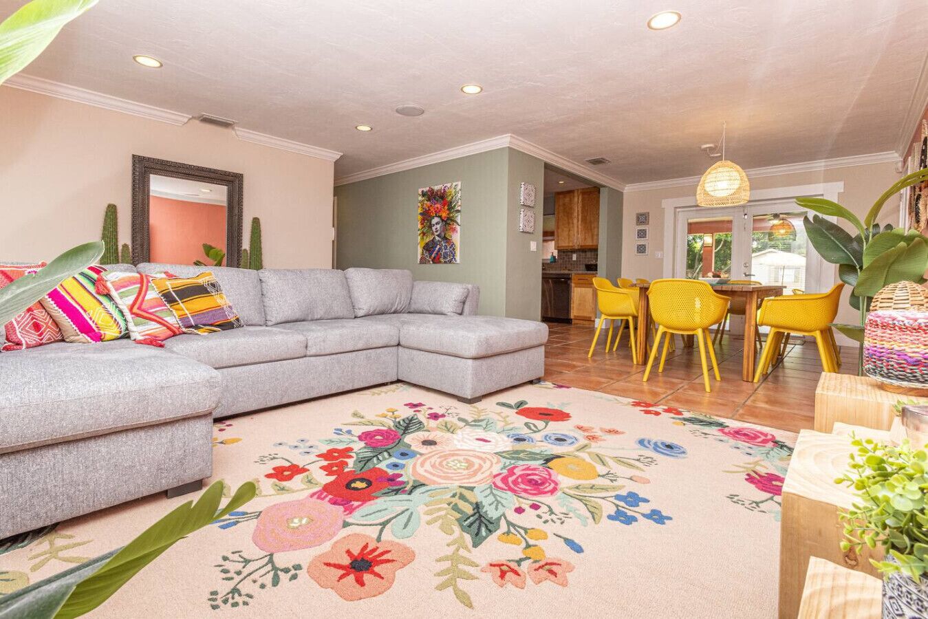 Un salon avec un canapé d’angle gris, des fauteuils jaunes et un tapis à motifs floraux.