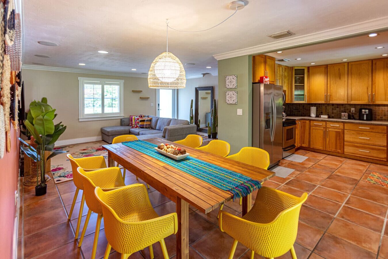 Un vaste espace de vie comprenant un coin repas avec une table en bois, des chaises jaunes, un canapé et une cuisine dotée de meubles en bois.