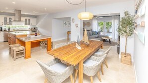 A modern kitchen with a central island, dining area with wicker chairs, and a living space with a sofa and a plant.