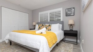 A neatly arranged bedroom with a bed, two bedside tables, a window with blinds, a closet, and a framed picture on the wall.
