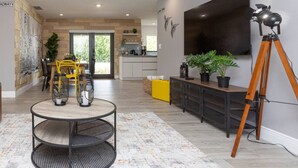 A modern living room with a round table, yellow chairs, a tripod, and a large TV on the wall.