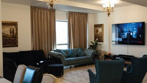 A living room with a sofa, chairs, a TV, and curtains. - Rovers Beach Hostel JBR (Dubai)