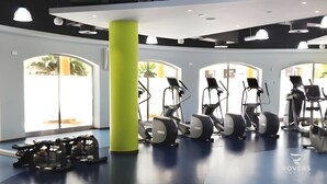 A modern gym with elliptical machines, a large green pillar, and a blue floor. - Rovers Beach Hostel JBR (Dubai)