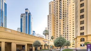 A hotel with a yellow facade, multiple floors, and a central courtyard with trees. - Rovers Beach Hostel JBR (Dubai)