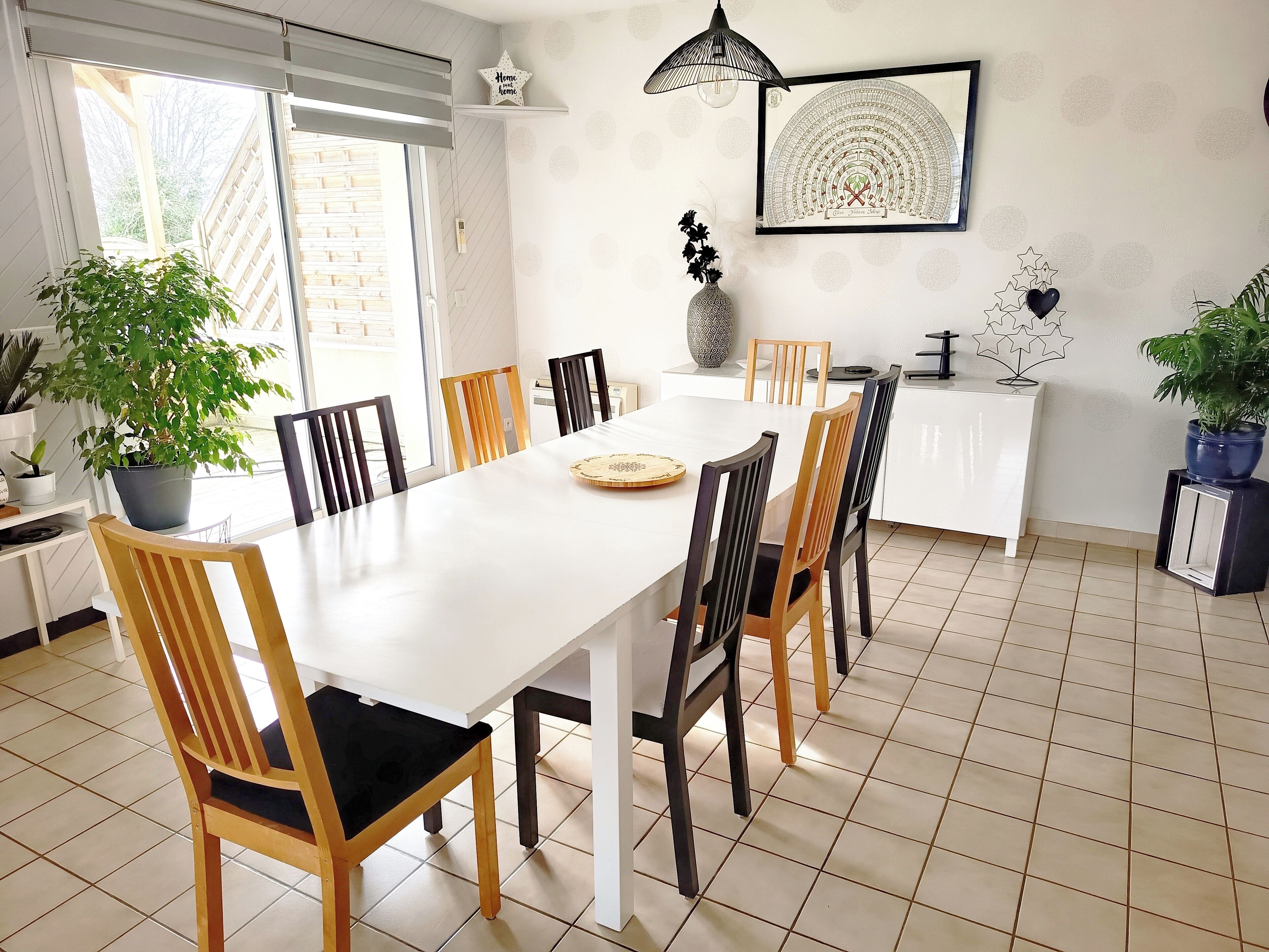 A dining area with a white table, wooden chairs, and a potted plant.