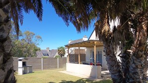 Un patio trasero con una pérgola de madera, una caseta para perros y un muro de piedra.