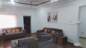 A spacious living room with two sofas, a glass coffee table, and a door leading to another room. -  Skenyo Hotel & Apartments (Abuja)