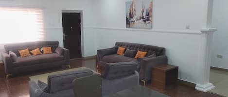 A spacious living room with two sofas, a glass coffee table, and a door leading to another room.