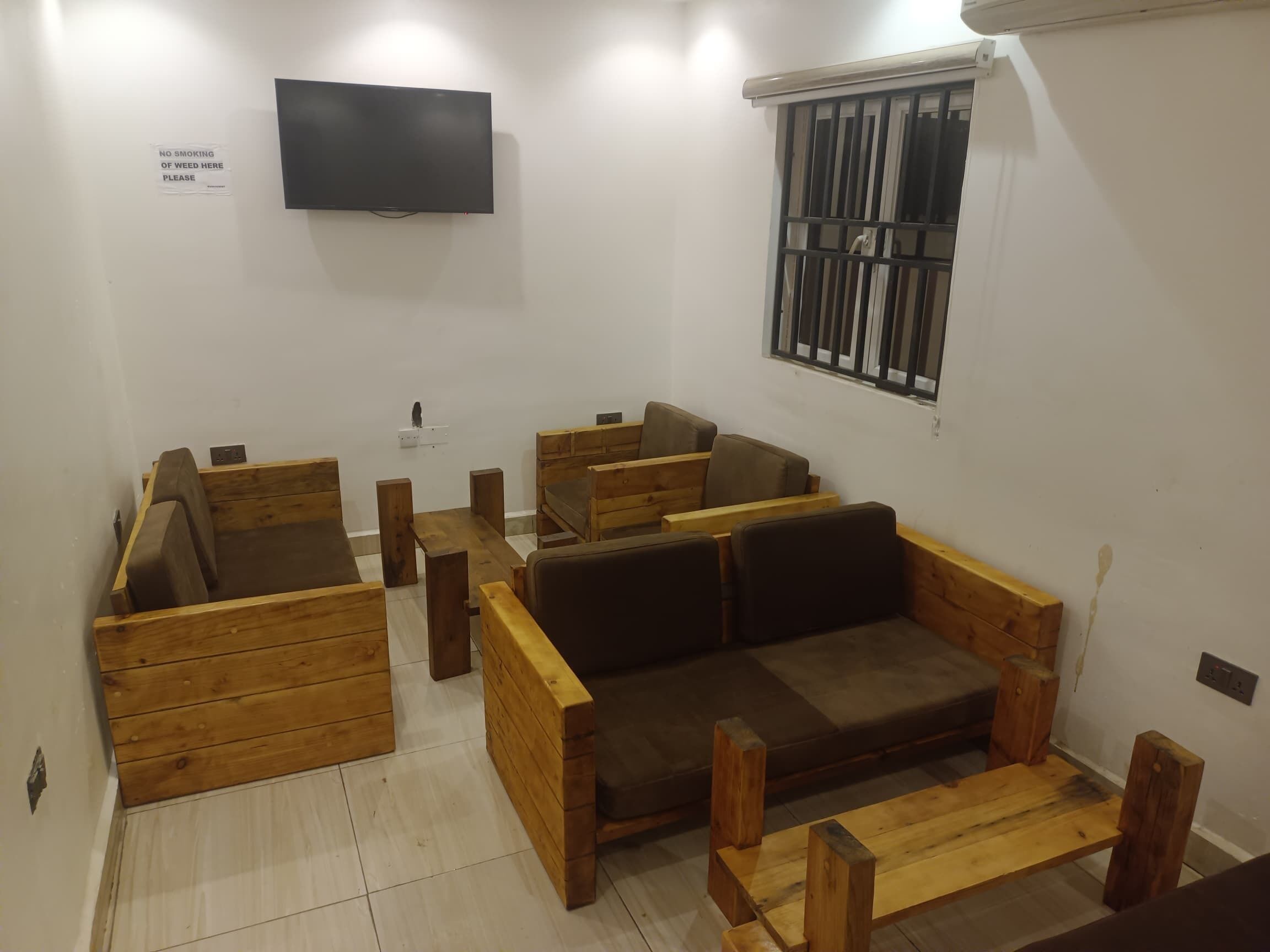 A modern living room with wooden furniture, a flat-screen TV, and a barred window.