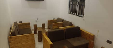 A modern living room with wooden furniture, a flat-screen TV, and a barred window.