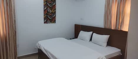 A bedroom with a single bed, beige curtains, a wall-mounted air conditioner, and a colorful abstract painting.