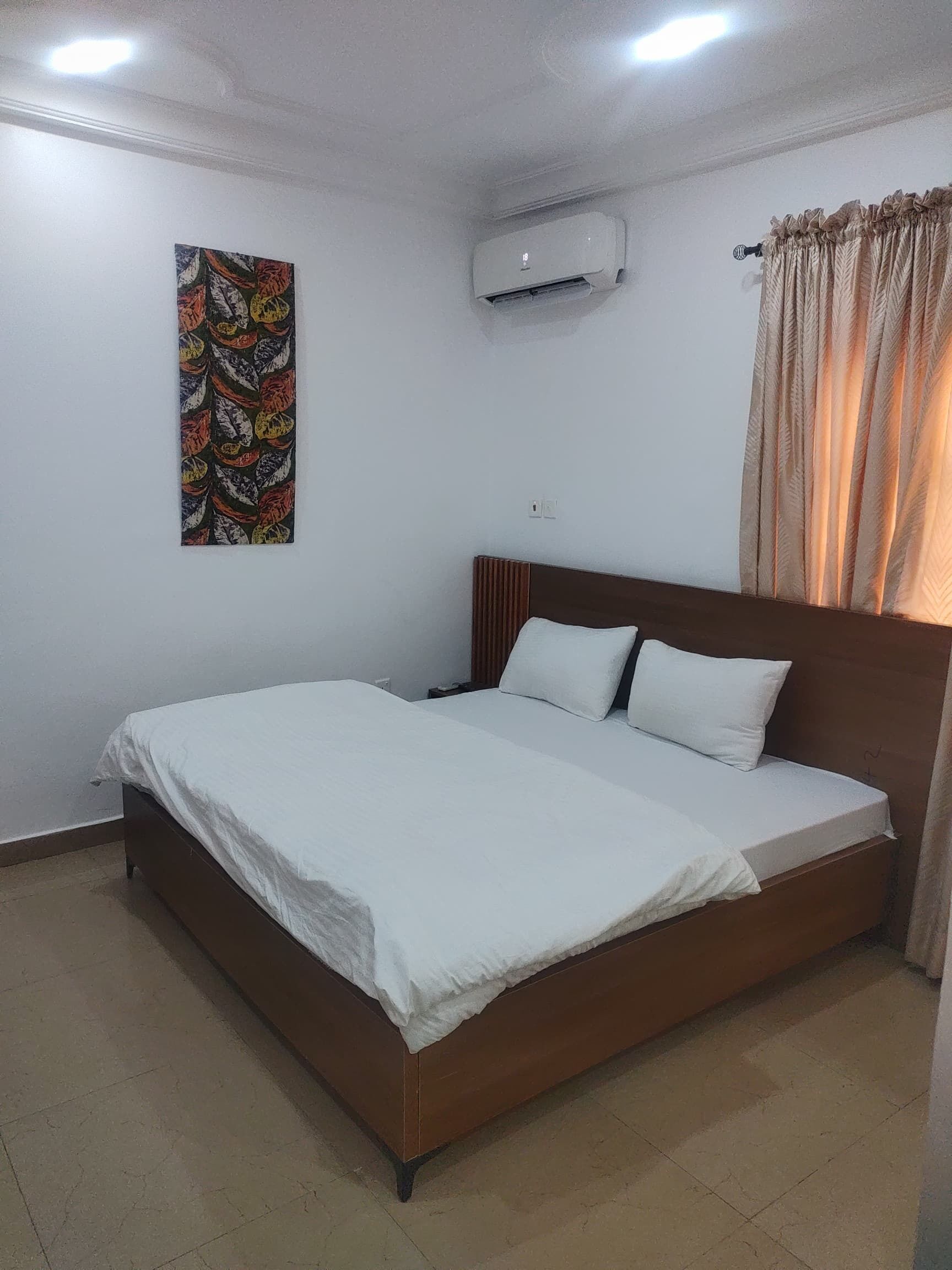 A bedroom with a single bed, a wall-mounted air conditioner, a ceiling light, and a curtain.
